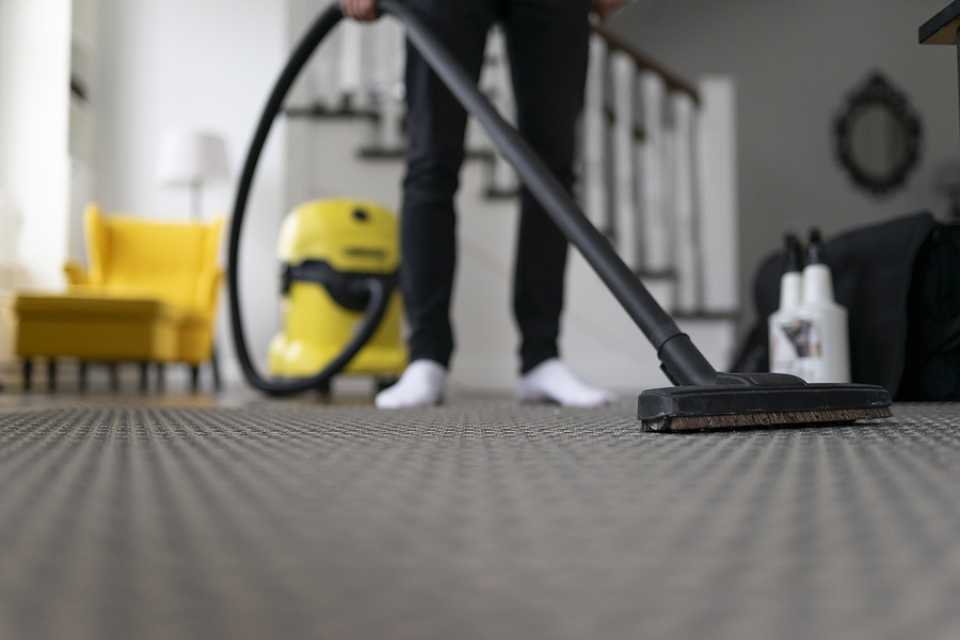 vacuuming grey patterned carpet in modern living room with yellow armchair